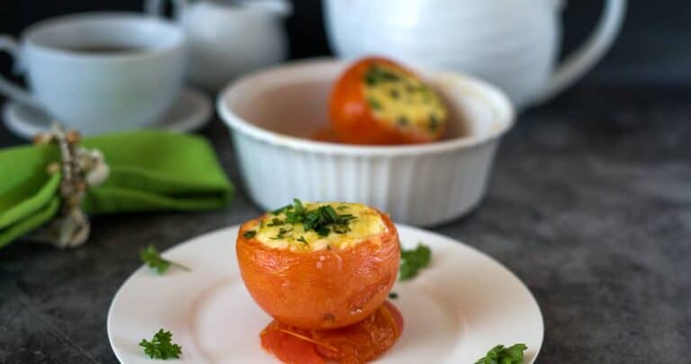 A stuffed tomato on a plate with breakfast crockery in the background