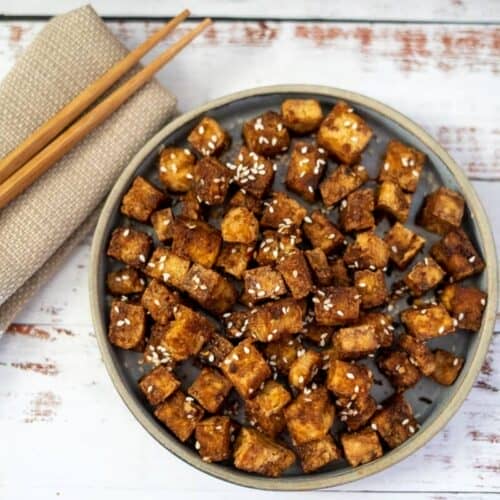 Crispy tofu in a bowl with chopsticks and sesame seeds, made in an air fryer.