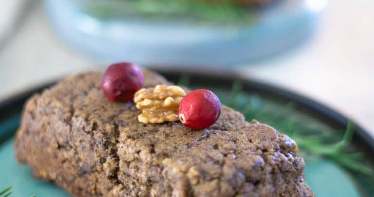 A cake with cranberries and sprigs of rosemary on a plate.